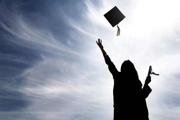 A black shadow of a graduate throwing their hat up into the air with a degree and sunny background.