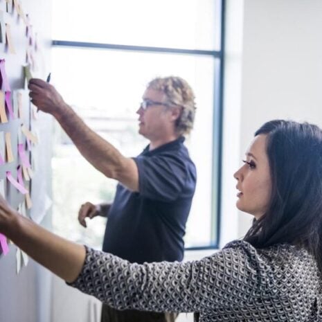 An office manager working with her colleague to put post it notes on a wall to organise their brainstorming session.