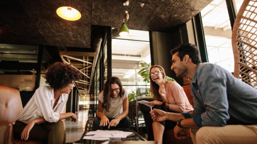 A group of four young creative professionals in a meeting in a modern, well-lit office. They are talking and laughing.
