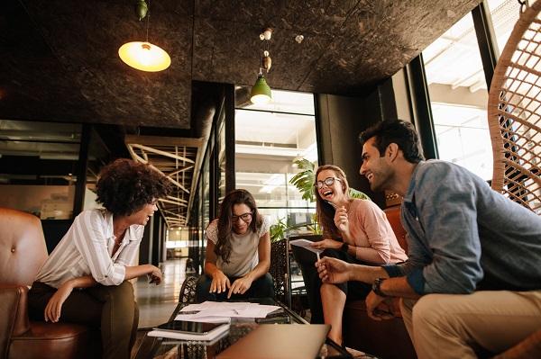 Four portfolio workers in an open plan office having a meeting while smiling and laughing.