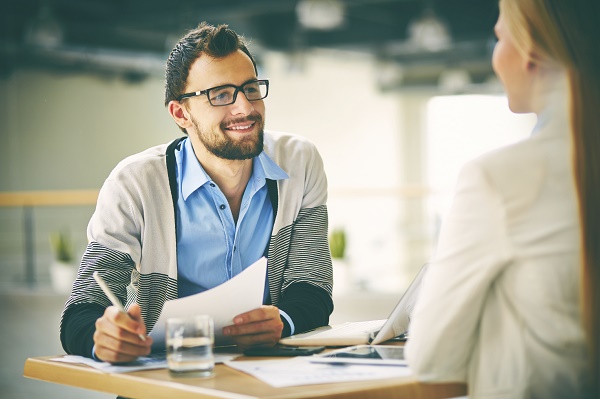 Smiling businessman taking notes while talking to a woman sat opposite