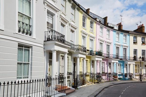 Colourful West End London houses in Primrose hill lined up. They are painted grey, yellow, pink, blue and beige.