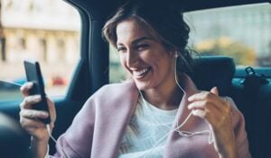 A private PA looking at her phone and smiling in a car while she's driven to the house of her principal.
