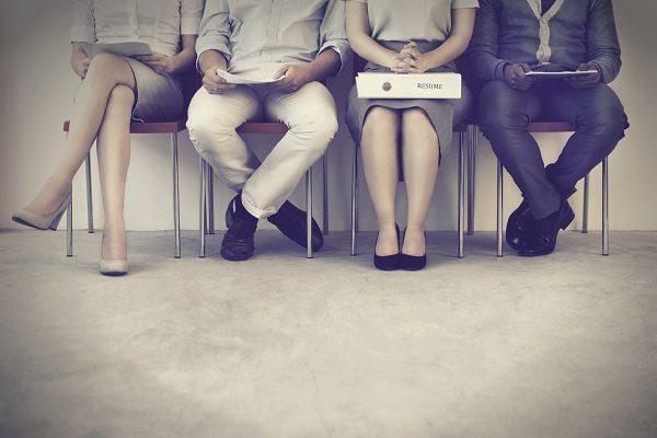 Four people dressed in business wear waiting along a wall for an interview opportunity.