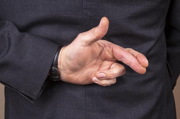 A business man’s hands in a ‘crossed fingers’ sign held behind his back.