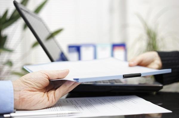 There’s a laptop on the table with two hands passing over a contract in a contract negotiation meeting.