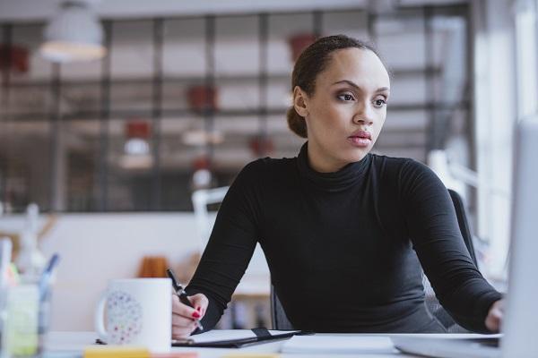 A woman looking at a desktop computer at a desk while resigning from her PA role and writing a handover.