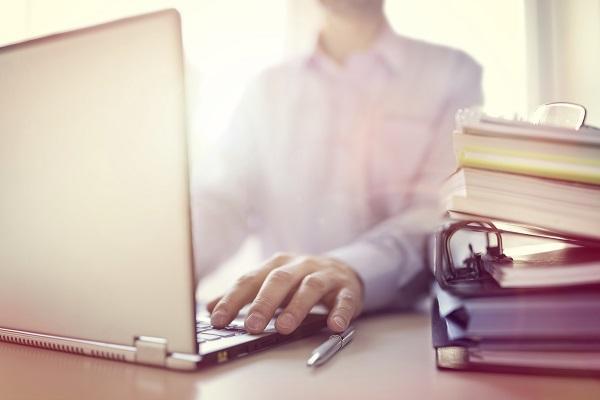 A close up of a businessman using a laptop to write job ads at his desk in a sunsoaked office.