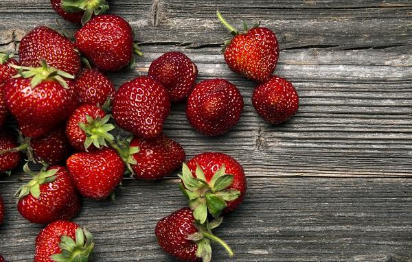 A pile of red strawberries on a wooden table, ready to be eaten.
