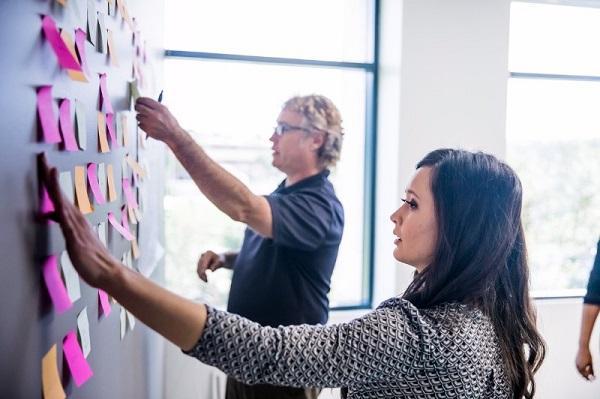 Two colleagues in a meeting using post it notes on a wall and discussing a project.