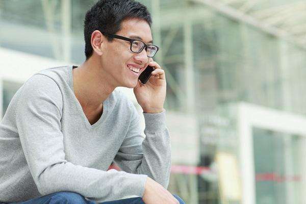 Man with glasses smiling while carrying out a telephone interview outside a building.