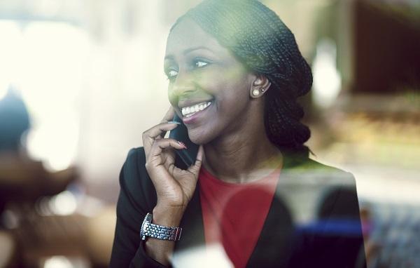 A virtual assistant on a phone through a glass window, smiling in a black jacket and red top.