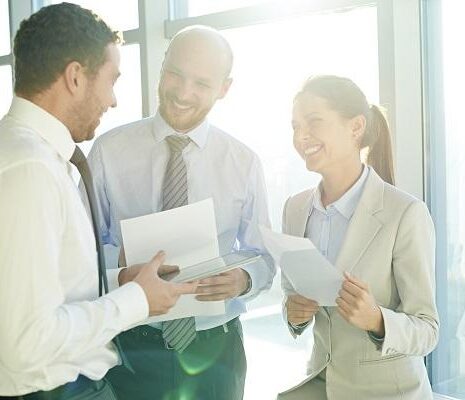 Three business colleagues talking and laughing in a sunlight room.