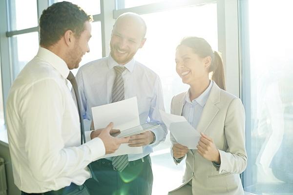 Three business colleagues talking and laughing in a sunlight room.