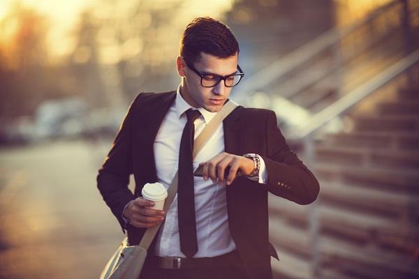 Man in a business suit in glasses looking at his watch while holding a coffee, running late for his job interview.