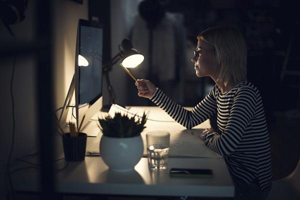A woman in a striped top and glasses looking for jobs on a computer after hours at her office.
