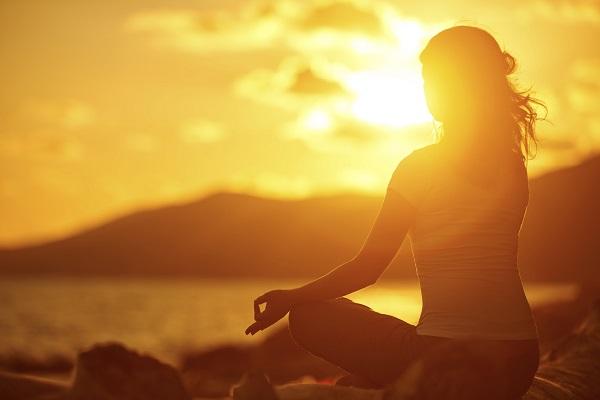 A woman in a relaxing yoga pose sitting on the beach in the sunset.