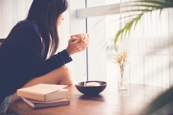 A business woman looking out a window while holding a cup of coffee, looking for her new job.