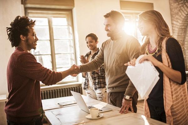 Three smiling people interviewing a confident man in a sunlit office.