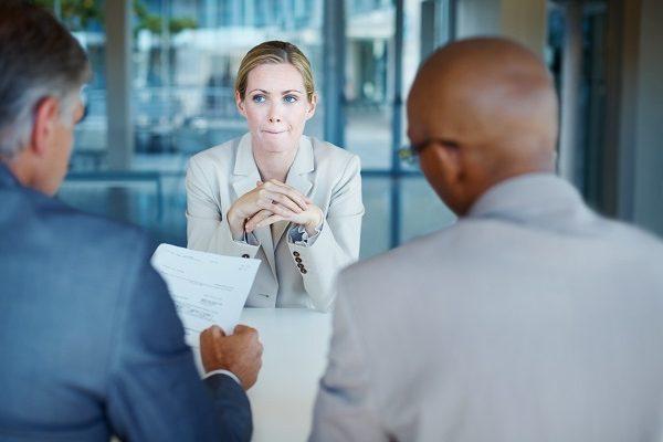 A sceptical woman in a job interview in a glass-walled office with a poorly prepared interviewer.