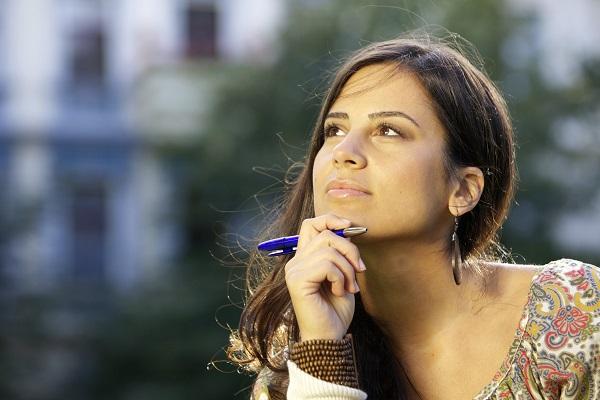 A woman holding a pen and looking off into the distance while thinking about settling into a new role.