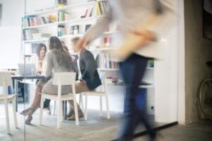 Group of creative people on a meeting in office, blurred motion of businessman passing in front, view through window
