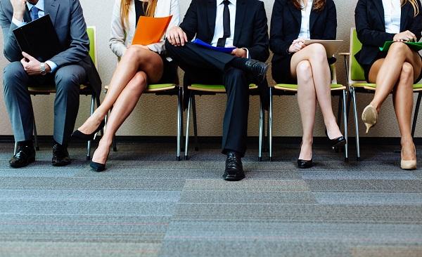 A shot of five candidates sitting in green chairs in business wear preparing for an interview.