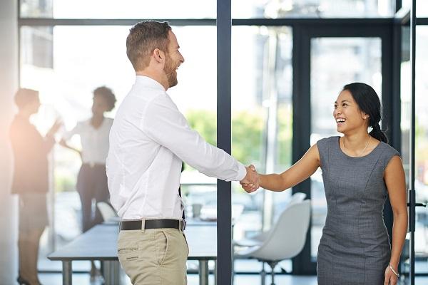 A successful recruiter shakes hands with her candidate in the foyer of a sunlit office.