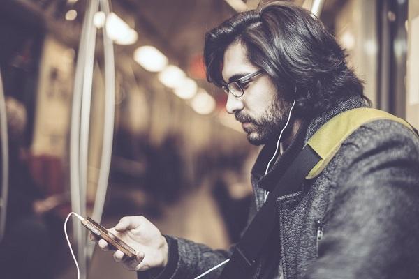 A man on public transport with headphones in and looking at his phone while researching into his employer.