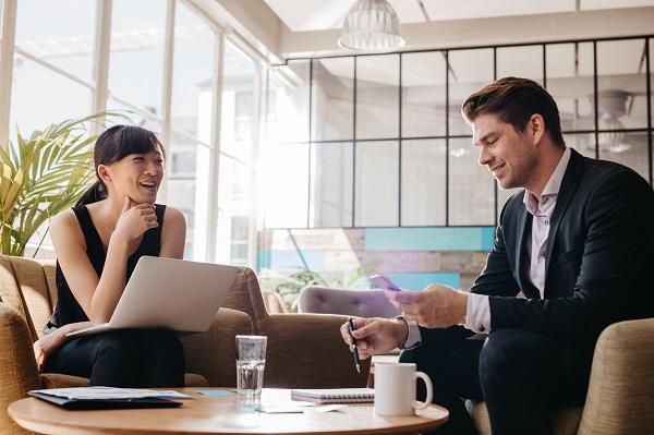 A private PA talks to a recruiter in a cool and modern open plan office while holding a laptop.