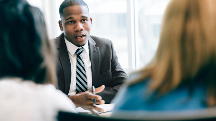 A man sat in a suit, addressing two business people sat in front of him