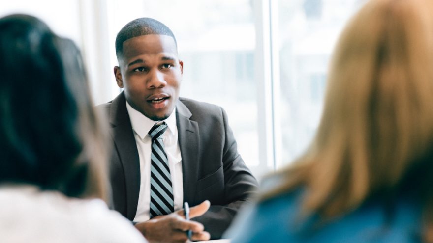 A man sat in a suit, addressing two business people sat in front of him