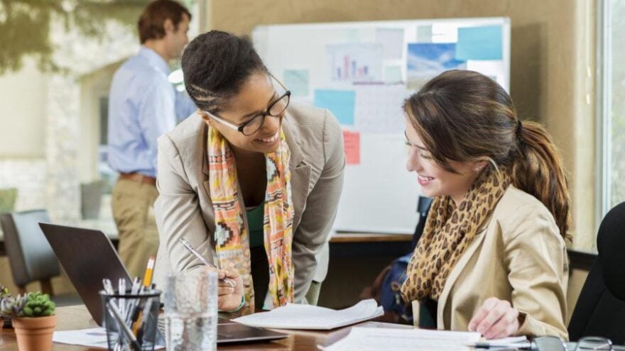 Cheerful businesswomen shows a temp worker the ropes in the office. They are reviewing documents