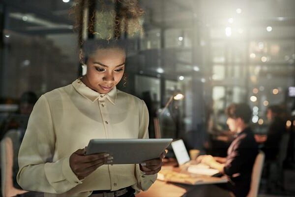 A female human resources professional is looking at a tablet while her colleagues work in the background after office hours.