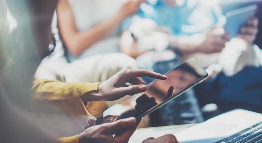 A temporary worker using a modern tablet with coworkers gathered together in the background.