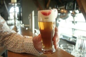 A photo of a man holding a full glass of beer at the bar, with a lipstick stain on it.