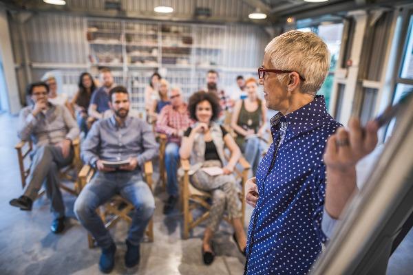 A woman presents a proposal in front of a room full of her colleagues, talking about the benefits of a boomerang hire.