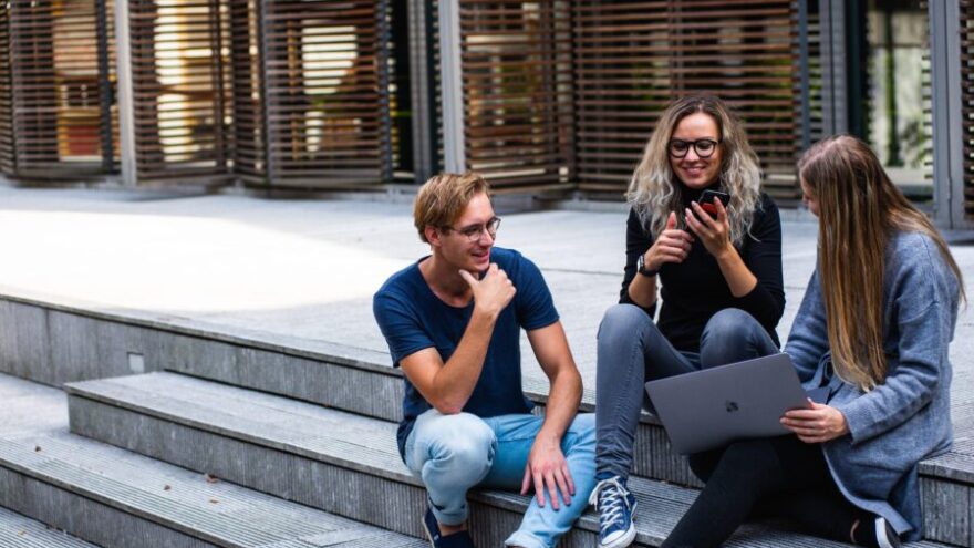 Three creative workers sit on the steps outside with a laptop