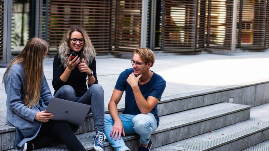Three creative workers sit on the steps outside with a laptop