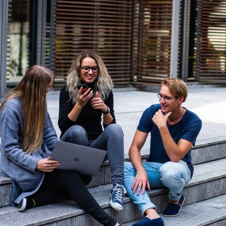 Three creative workers sit on the steps outside with a laptop for tech hiring agency in dubai