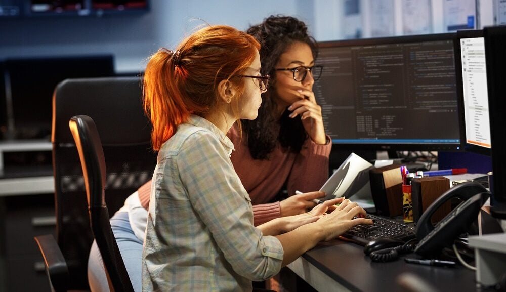 Two women working on a programming project in an office.