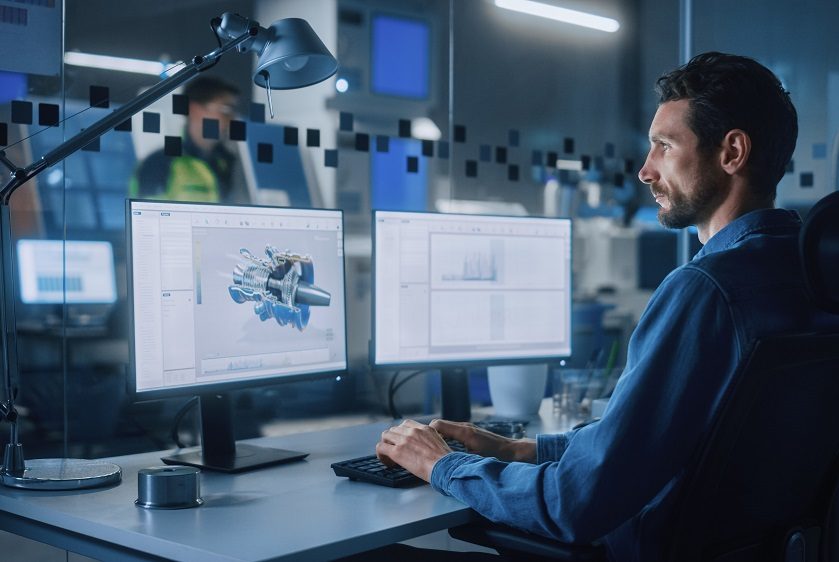 A digital designer working on a project on two computers in an office.