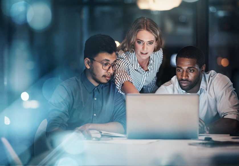 Three IT colleagues working together around a computer.