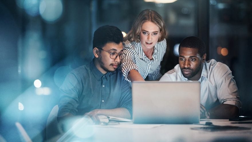 Three IT colleagues working together around a computer.