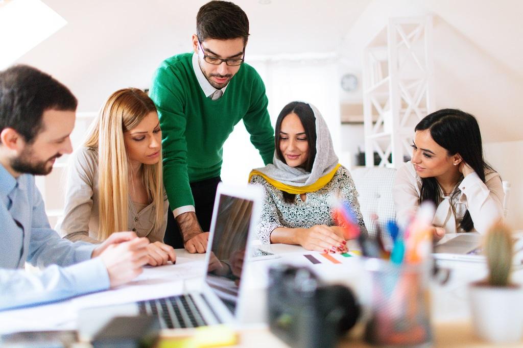Photo of a young team working together in the modern office - consulting each other about some issue while sitting around their company's charts