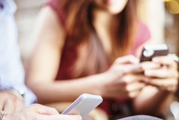 A closeup of a man holding a phone and using social media with a woman in the background.