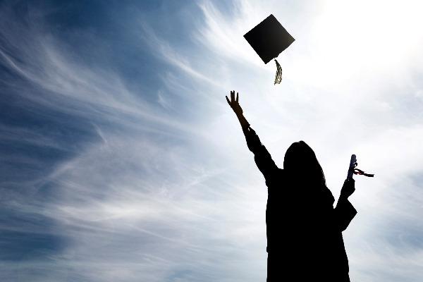 A shadow of a graduate in a cap and gown, throwing her hat into the air on a sunny day.