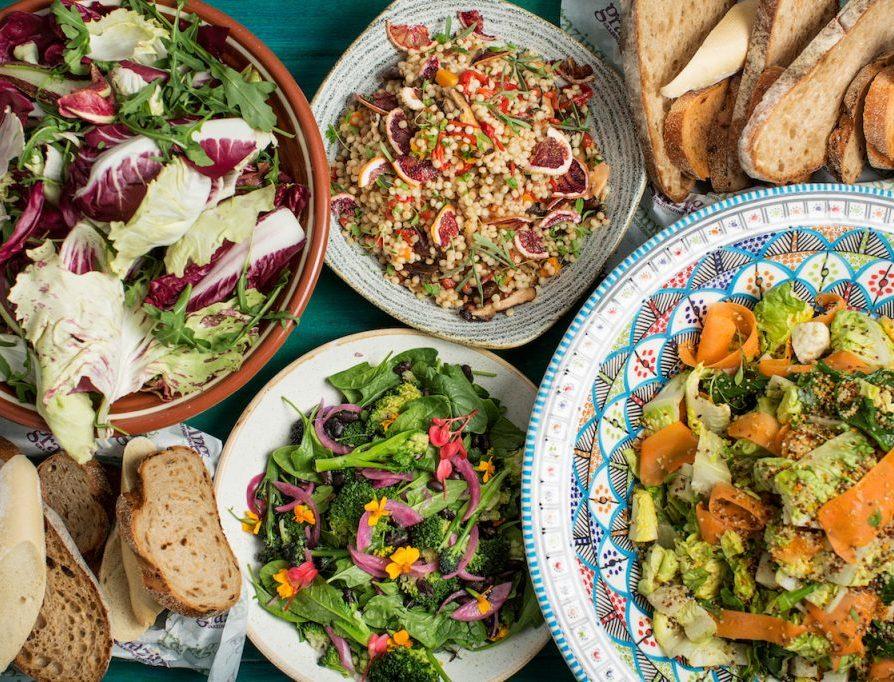 Various plates of catered lunch sitting on a tablecloth, with salads, bread and other delicious dishes.