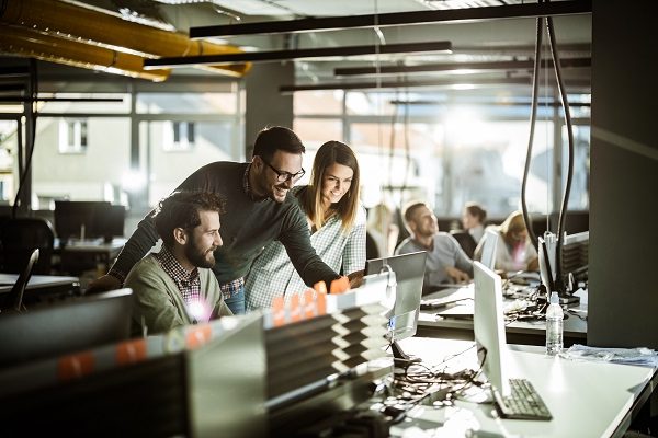 A group of IT colleagues working together around a computer in a busy office.