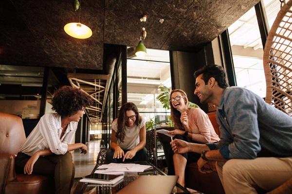 Four smiling colleagues talking in an informal, modern setting.